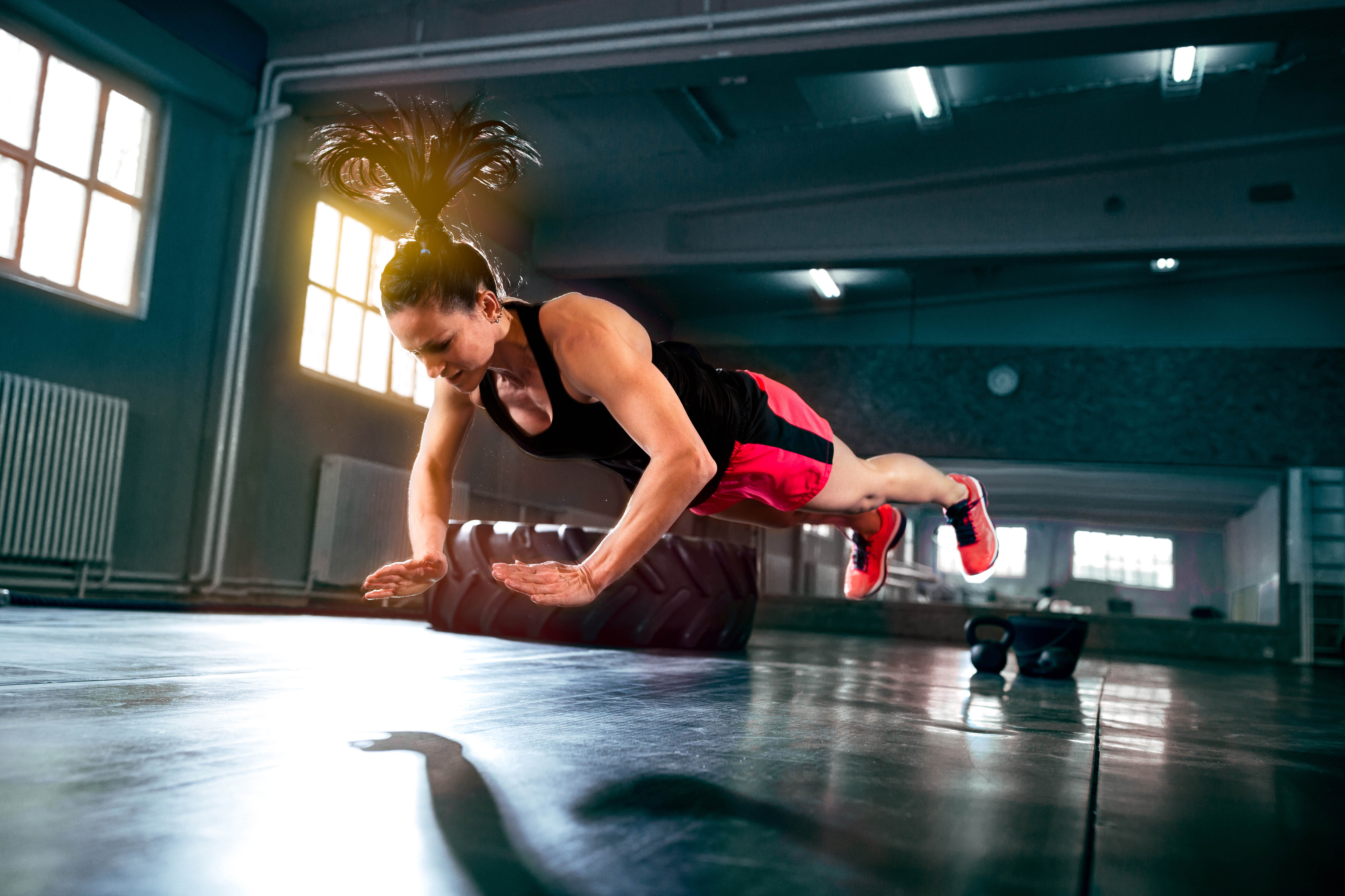 Young, fit woman mid-flight during a clapping push-up. Background is a gym, light streaming in through the window. Young, fit woman mid-flight during a clapping push-up. Background is a gym, light streaming in through the window.
